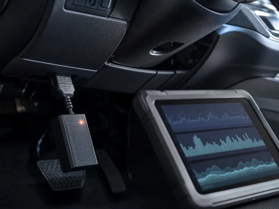 Диагностический сканер подключён к разъёму OBD-II автомобиля, рядом открыт экран с графиками